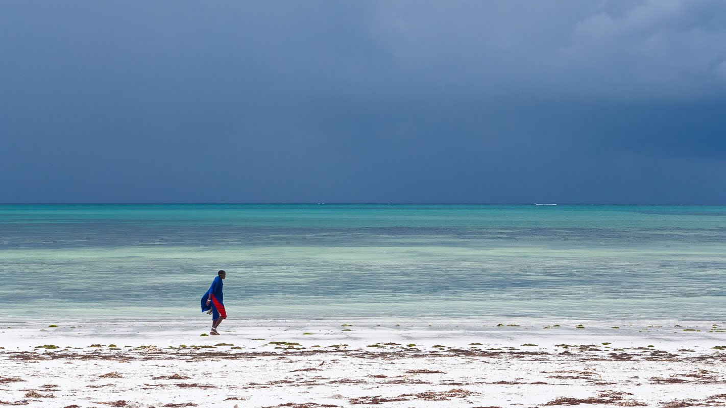 Een masai loopt op het strand van Zanzibar